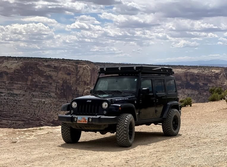 Side profile of a Jeep Wrangler JK Rubicon at a canyon overlook, Front Runner Slimline II roof rack with hard-shell rooftop tent compactly stowed on top.