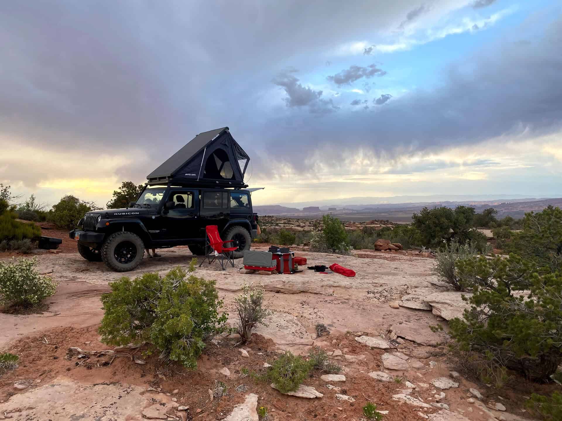 Jeep Wrangler JK Rubicon at a Moab desert overlook with a hard-shell rooftop tent deployed on the Front Runner Slimline II Extreme roof rack