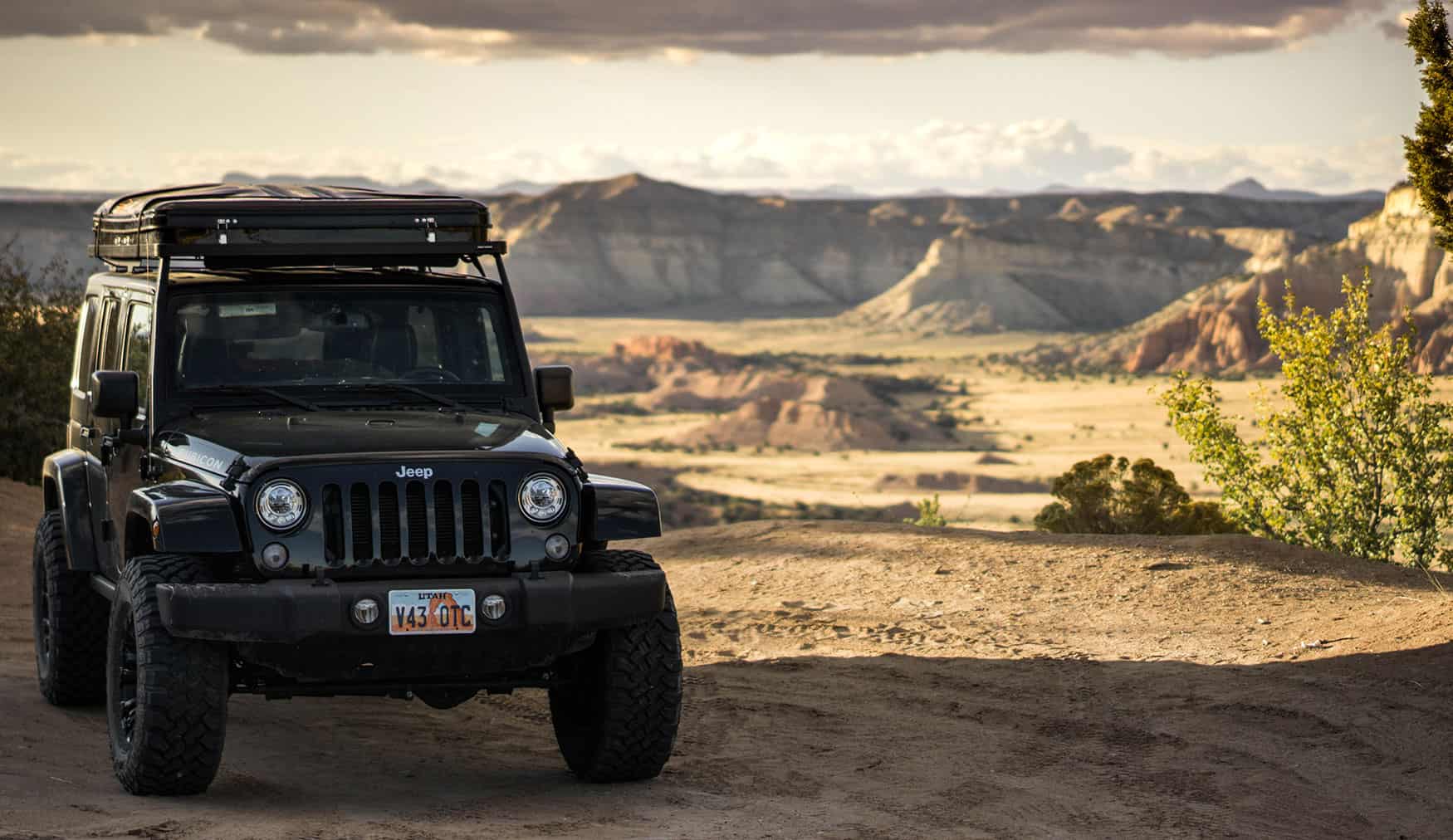Jeep Wrangler JK Rubicon at a Utah desert overlook at golden hour, Front Runner Slimline II roof rack with hard-shell rooftop tent stowed, expansive red rock canyon country in the background.